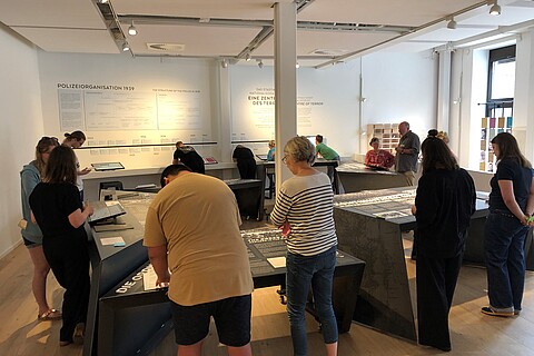 Viele Personen stehen in einem Ausstellungsraum und lesen Ausstellungstexte. 